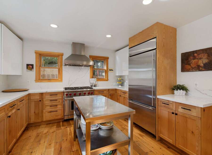 This spacious kitchen boasts modern stainless steel appliances, including a professional-grade range and a large refrigerator, complemented by warm, natural wood cabinetry.