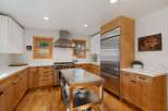 This spacious kitchen boasts modern stainless steel appliances, including a professional-grade range and a large refrigerator, complemented by warm, natural wood cabinetry.