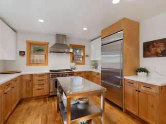 This spacious kitchen boasts modern stainless steel appliances, including a professional-grade range and a large refrigerator, complemented by warm, natural wood cabinetry.