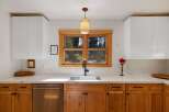 This modern kitchen features sleek white upper cabinets contrasted with warm, natural wood lower cabinets and drawers.