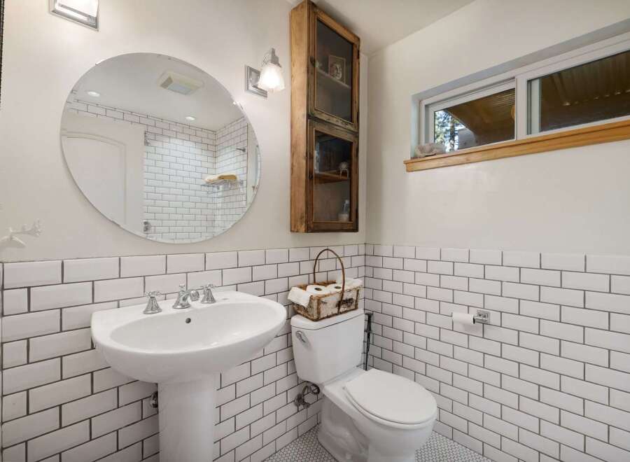 This charming bathroom features a classic subway tile design, a pedestal sink, and a convenient toilet with a decorative basket.