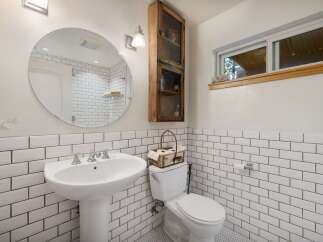 This charming bathroom features a classic subway tile design, a pedestal sink, and a convenient toilet with a decorative basket.