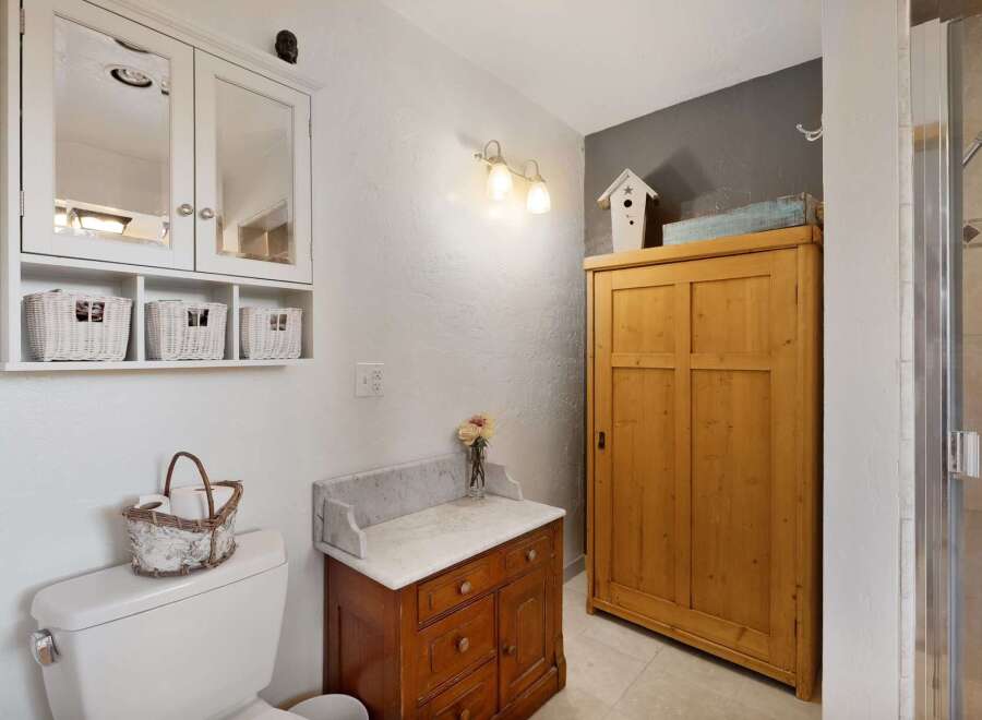 This charming bathroom features a white medicine cabinet with mirrored doors and three woven baskets for storage.