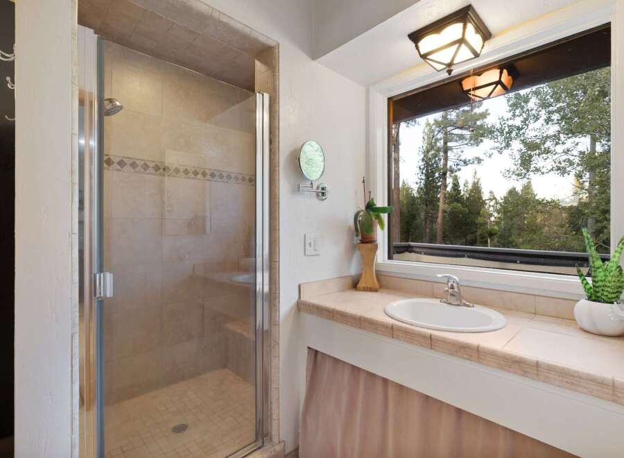 Experience serene living with this charming bathroom featuring a spacious glass-enclosed shower and a vanity with a large window offering breathtaking forest views.