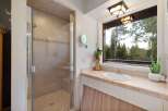 Experience serene living with this charming bathroom featuring a spacious glass-enclosed shower and a vanity with a large window offering breathtaking forest views.