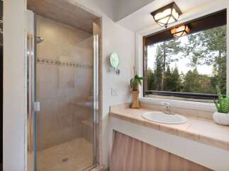 Experience serene living with this charming bathroom featuring a spacious glass-enclosed shower and a vanity with a large window offering breathtaking forest views.