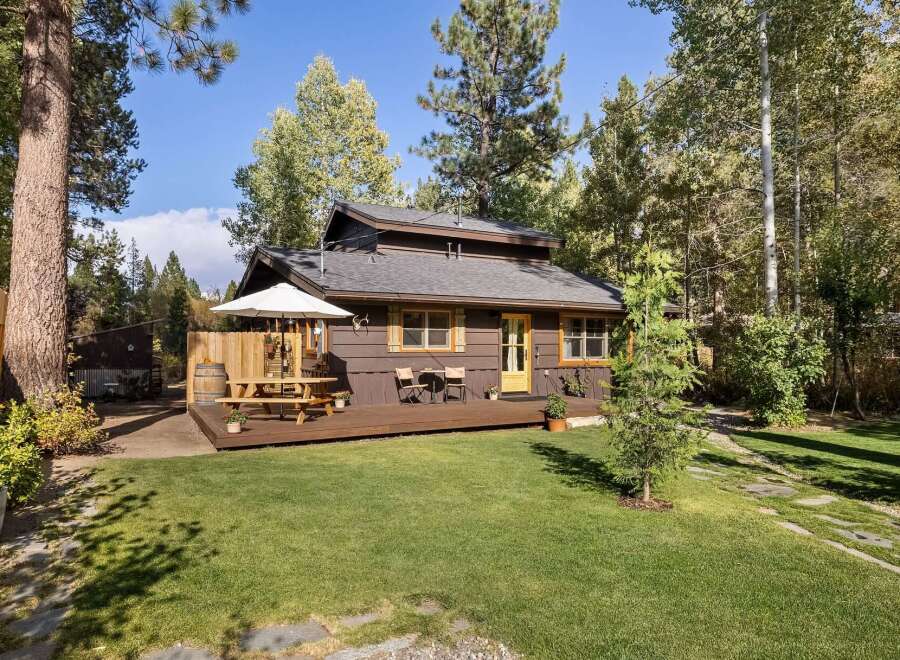 Charming cabin nestled among mature trees, featuring a spacious wooden deck perfect for outdoor dining and relaxation.