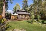 Charming cabin nestled among mature trees, featuring a spacious wooden deck perfect for outdoor dining and relaxation.
