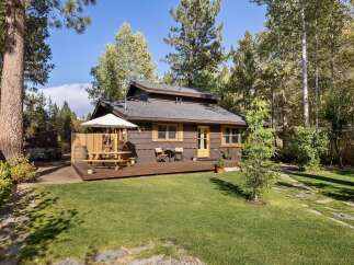 Charming cabin nestled among mature trees, featuring a spacious wooden deck perfect for outdoor dining and relaxation.