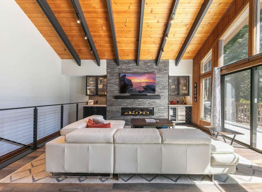 Experience modern living in this stunning great room, featuring a vaulted wood-paneled ceiling with exposed beams and a sleek stone fireplace.