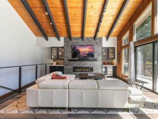 Experience modern living in this stunning great room, featuring a vaulted wood-paneled ceiling with exposed beams and a sleek stone fireplace.