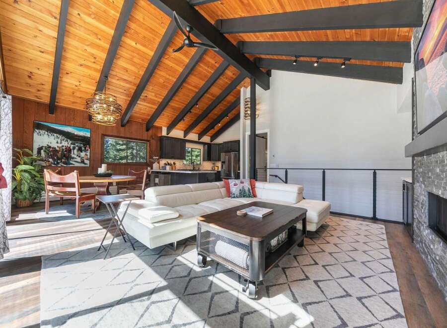 Experience modern mountain living in this stunning open-concept great room, featuring a vaulted wood-paneled ceiling with exposed beams and a cozy stone fireplace.