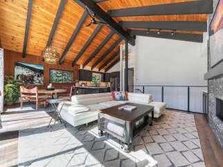 Experience modern mountain living in this stunning open-concept great room, featuring a vaulted wood-paneled ceiling with exposed beams and a cozy stone fireplace.