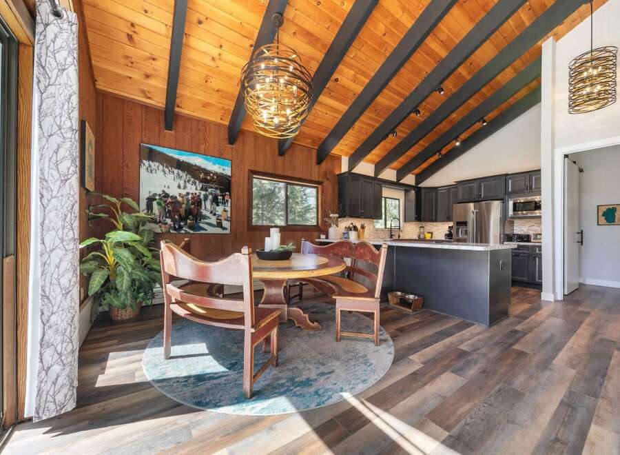Experience rustic charm in this open-concept living space, featuring a vaulted wood-paneled ceiling with exposed beams and a striking modern chandelier.