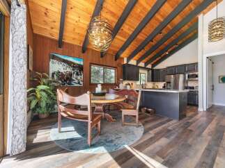 Experience rustic charm in this open-concept living space, featuring a vaulted wood-paneled ceiling with exposed beams and a striking modern chandelier.