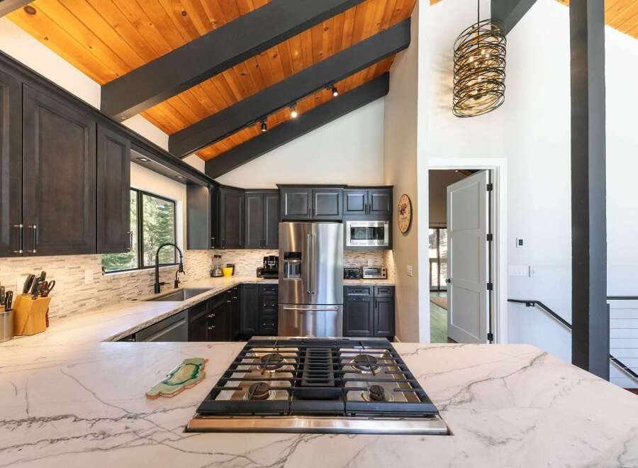Experience modern mountain living in this stunning kitchen, featuring dark cabinetry, a sleek marble countertop, and a professional gas range.