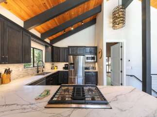 Experience modern mountain living in this stunning kitchen, featuring dark cabinetry, a sleek marble countertop, and a professional gas range.