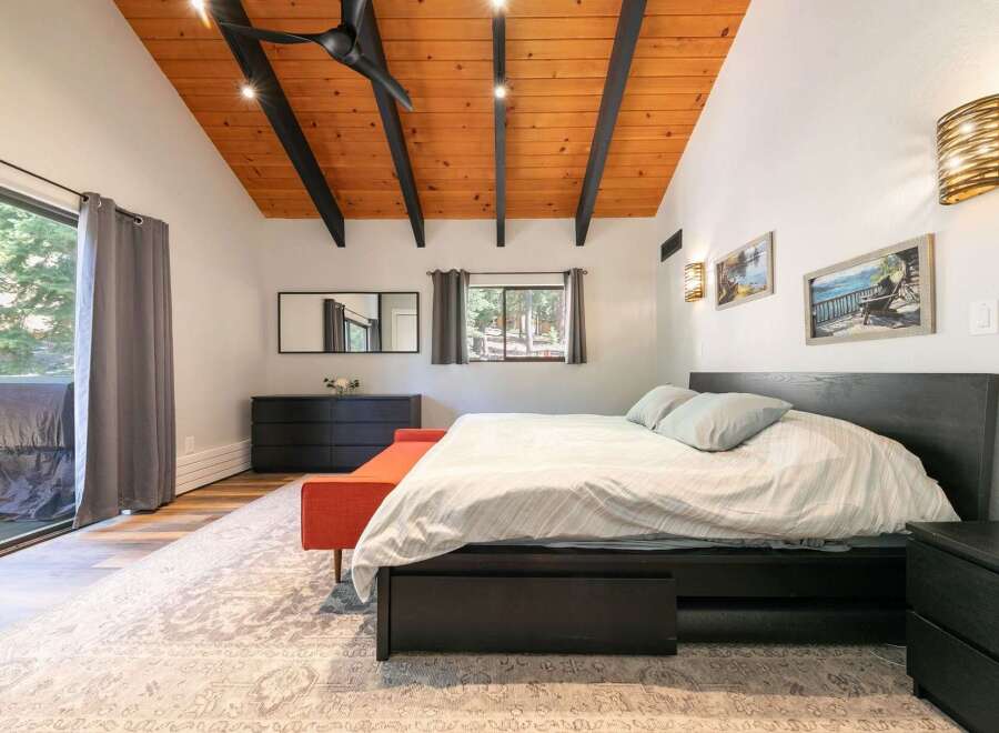 Experience rustic charm in this inviting bedroom featuring a vaulted wood-paneled ceiling with exposed beams and modern lighting.