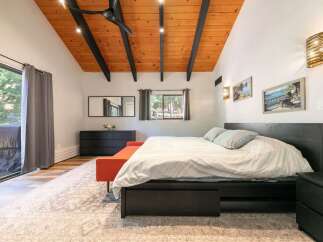 Experience rustic charm in this inviting bedroom featuring a vaulted wood-paneled ceiling with exposed beams and modern lighting.