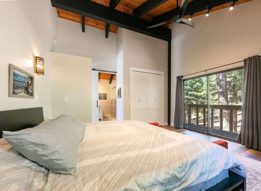 Experience serene living in this charming bedroom featuring a vaulted ceiling with exposed wood beams and a modern black fan.