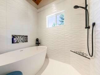 Experience modern luxury in this stunning bathroom featuring a freestanding soaking tub and a sleek, wave-patterned tile design.