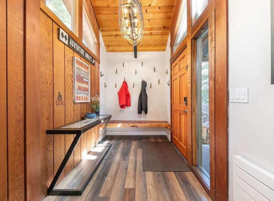 Step into a warm and inviting entryway featuring rustic wood paneling and a vaulted ceiling with a striking modern chandelier.