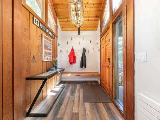 Step into a warm and inviting entryway featuring rustic wood paneling and a vaulted ceiling with a striking modern chandelier.