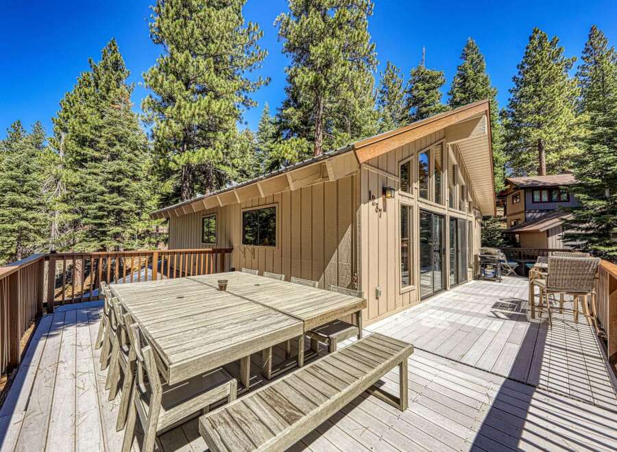 Enjoy outdoor living and dining on this expansive wooden deck, perfect for entertaining guests amidst a serene forest setting.