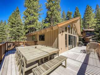 Enjoy outdoor living and dining on this expansive wooden deck, perfect for entertaining guests amidst a serene forest setting.