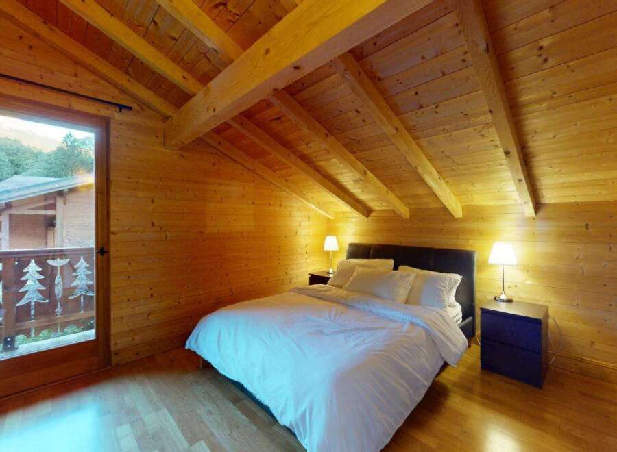 Experience rustic charm in this cozy wooden cabin bedroom, featuring a comfortable bed with crisp white linens and a private balcony overlooking a scenic mountain view.
