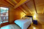 Experience rustic charm in this cozy wooden cabin bedroom, featuring a comfortable bed with crisp white linens and a private balcony overlooking a scenic mountain view.