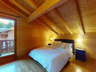 Experience rustic charm in this cozy wooden cabin bedroom, featuring a comfortable bed with crisp white linens and a private balcony overlooking a scenic mountain view.