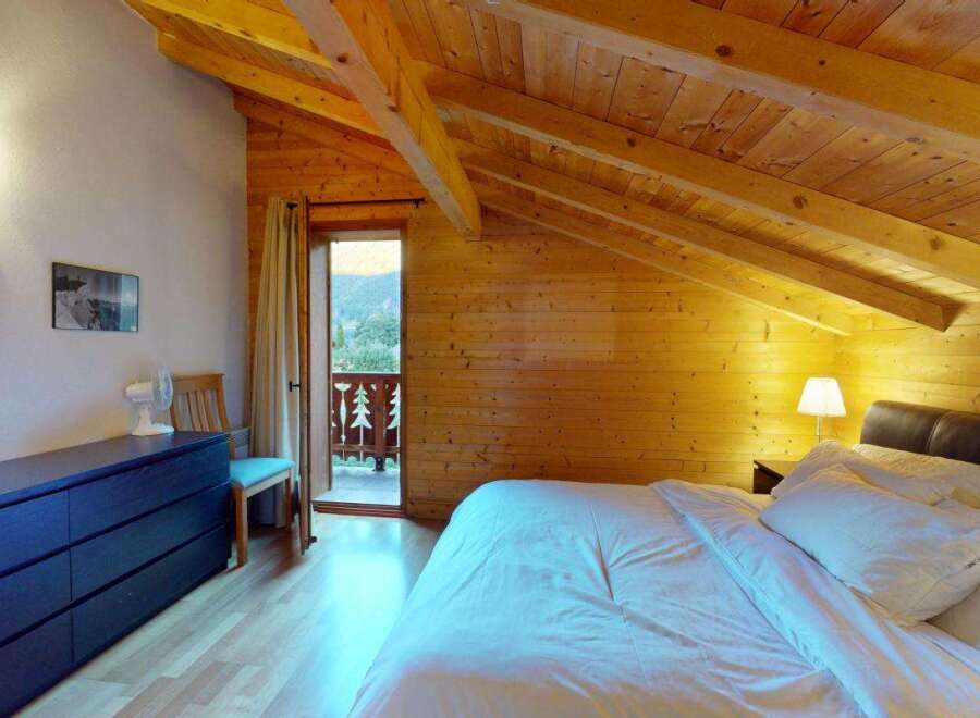 Experience cozy mountain living in this charming attic bedroom, featuring exposed wooden beams and a warm, inviting ambiance.
