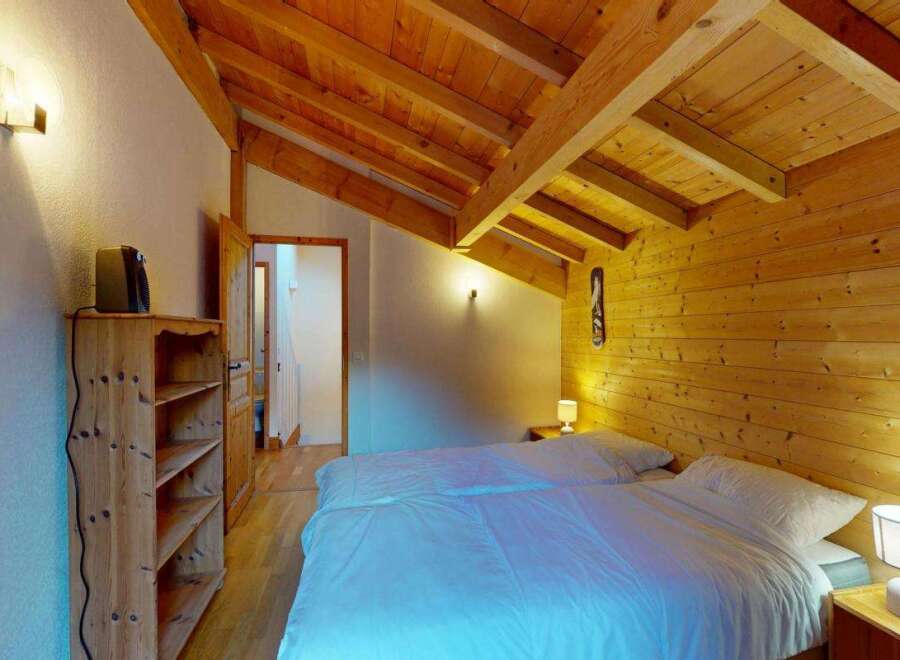 Experience cozy mountain living in this charming bedroom featuring a sloped wooden beam ceiling and warm wood-paneled walls.