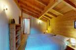 Experience cozy mountain living in this charming bedroom featuring a sloped wooden beam ceiling and warm wood-paneled walls.