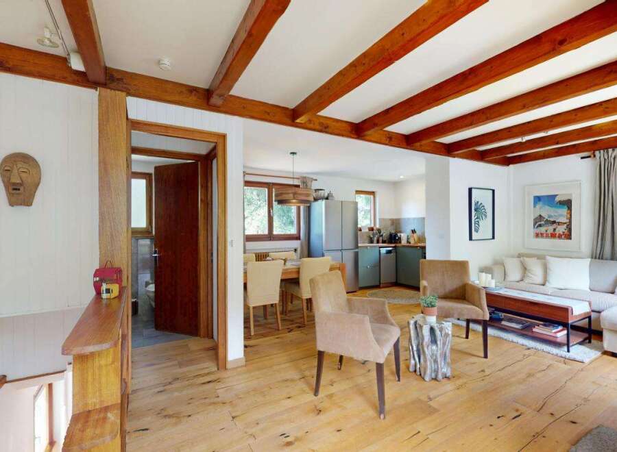 Experience rustic charm in this inviting open-plan living space, featuring exposed wooden beams and a warm, natural wood floor.