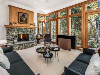 Experience luxurious living in this stunning great room, featuring a magnificent stone fireplace and expansive floor-to-ceiling windows that offer breathtaking views of the surrounding forest.
