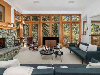 Experience the ultimate in rustic luxury with this stunning living room, featuring a magnificent stone fireplace and floor-to-ceiling windows that offer breathtaking views of the surrounding forest.