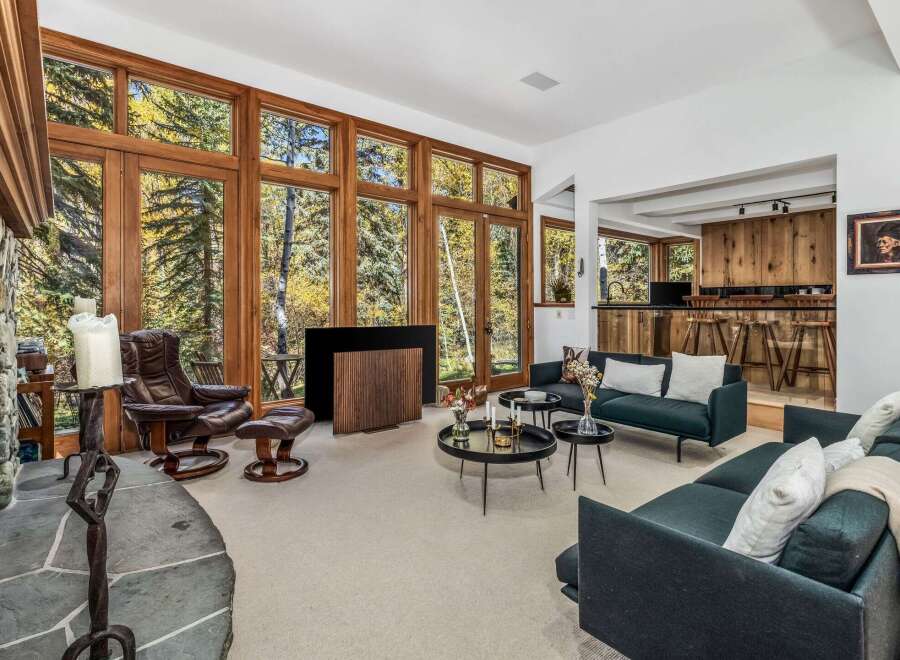 Experience breathtaking natural beauty from this stunning living room, featuring floor-to-ceiling windows that offer panoramic views of the surrounding autumn foliage.