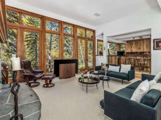Experience breathtaking natural beauty from this stunning living room, featuring floor-to-ceiling windows that offer panoramic views of the surrounding autumn foliage.