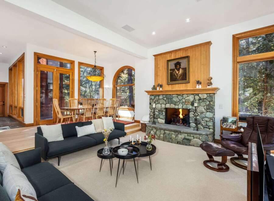 Experience rustic elegance in this spacious living area, featuring a grand stone fireplace and abundant natural light from large wooden-framed windows.