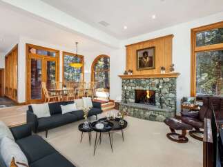 Experience rustic elegance in this spacious living area, featuring a grand stone fireplace and abundant natural light from large wooden-framed windows.