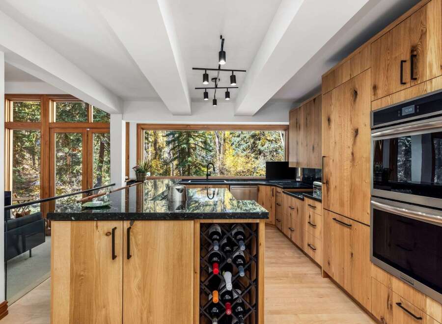 Experience luxury living in this stunning modern kitchen, featuring custom natural wood cabinetry and a sleek black granite countertop.