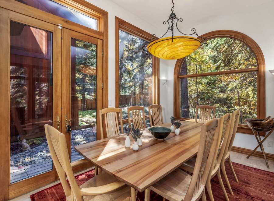 Experience seamless indoor-outdoor living with this elegant dining room, featuring expansive wooden-framed glass doors that open to a serene, stone-paved patio and lush greenery.