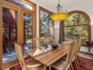 Experience seamless indoor-outdoor living with this elegant dining room, featuring expansive wooden-framed glass doors that open to a serene, stone-paved patio and lush greenery.