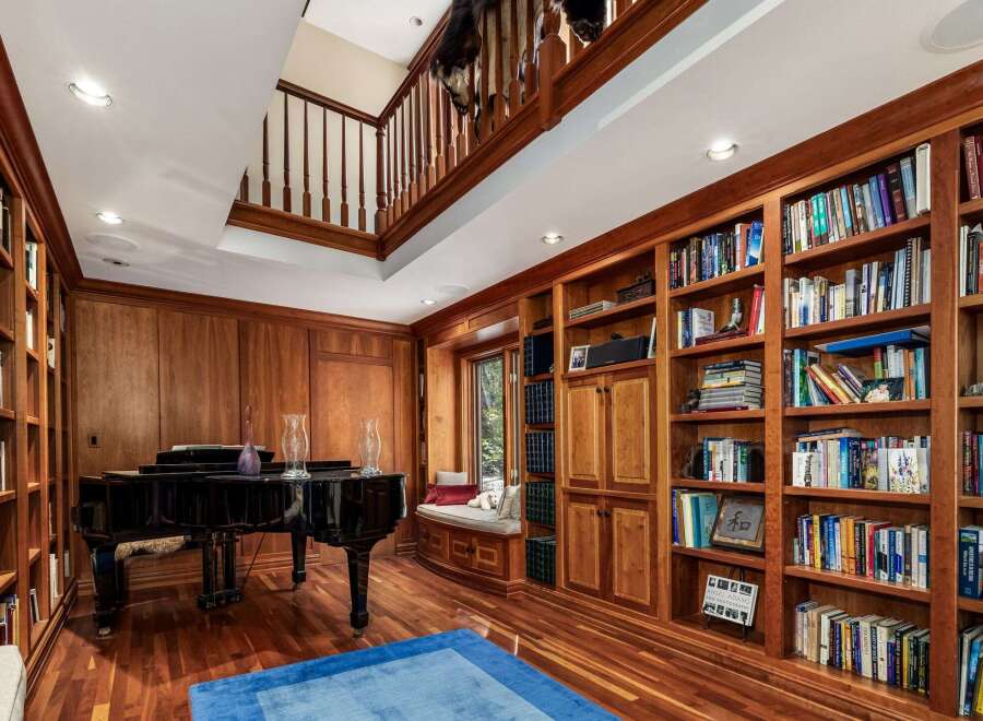 Step into this luxurious library, featuring rich wood paneling and floor-to-ceiling bookshelves filled with a diverse collection.