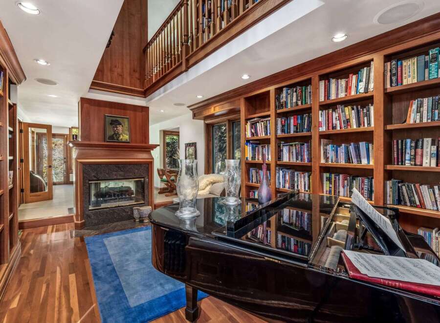 This luxurious living room features a grand piano, a cozy fireplace, and extensive built-in bookshelves, creating an elegant and inviting atmosphere.