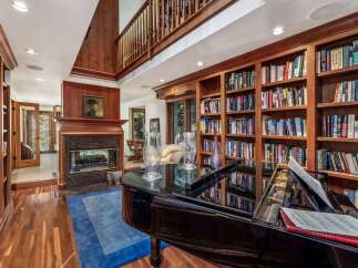 This luxurious living room features a grand piano, a cozy fireplace, and extensive built-in bookshelves, creating an elegant and inviting atmosphere.
