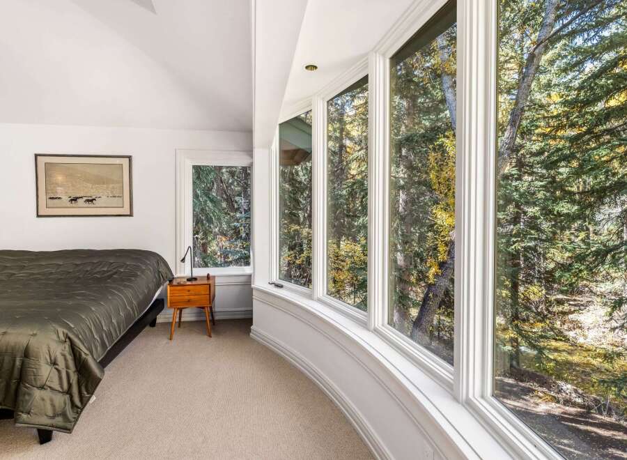 Experience breathtaking natural beauty from this bedroom, featuring expansive bay windows that offer panoramic views of a serene forest and a flowing creek.
