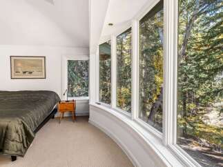 Experience breathtaking natural beauty from this bedroom, featuring expansive bay windows that offer panoramic views of a serene forest and a flowing creek.